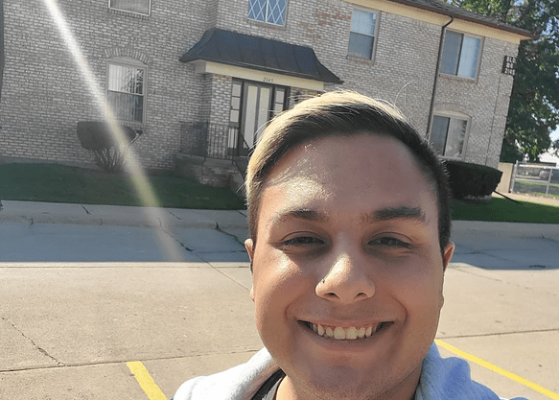 Selfie of smiling young man, in front of apartment building.