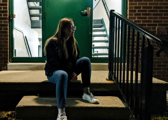 Young woman sitting on steps of apartment building in evening hours